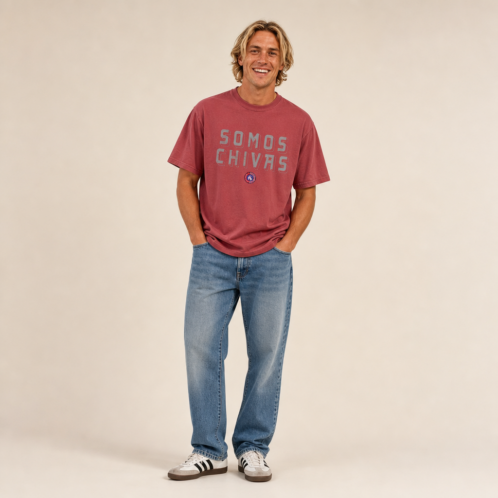 Man wearing the Lindale Chivas Somos Chivas Tee in Crimson, relaxed fit, worn untucked over jeans with Adidas Sambas
